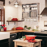 A picture of a kitchen. There's a double oven, butler sink, extractor hood, window, a plate rack and a small wooden trolley that has a crock pot on it, alongside some carrots