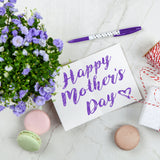 Some purple flowers, a present and some macaroons with a sign that says, 'Happy Mother's Day'