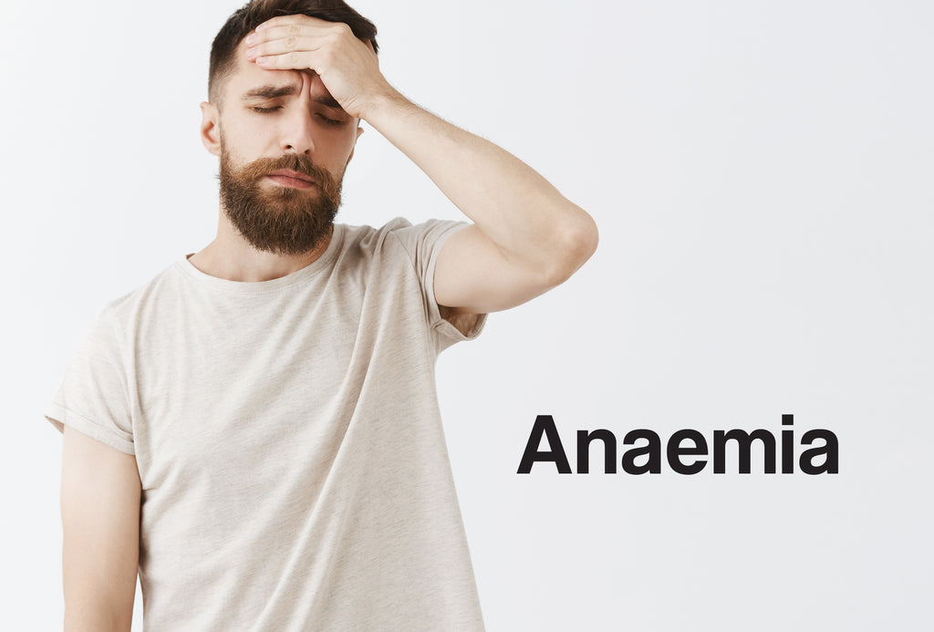 A bearded, pale man in an off-white t-shirt; he has his left hand to his forehead and looks unwell and slightly dizzy. The word – Anaemia – can be seen