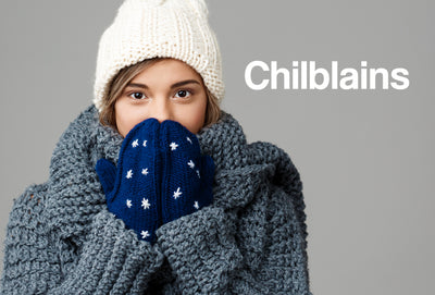 A young lady wearing a very thick jumper. She also has gloves and a hat on. She is holding her hands to her face, as though she is very cold. The word – Chilblains – can be seen
