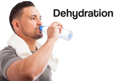 A man in his 30s, wearing a grey t-shirt, has a white towel around his shoulders, as though just having worked out. He is drinking from a bottle of water. The word – Dehydration – is showing