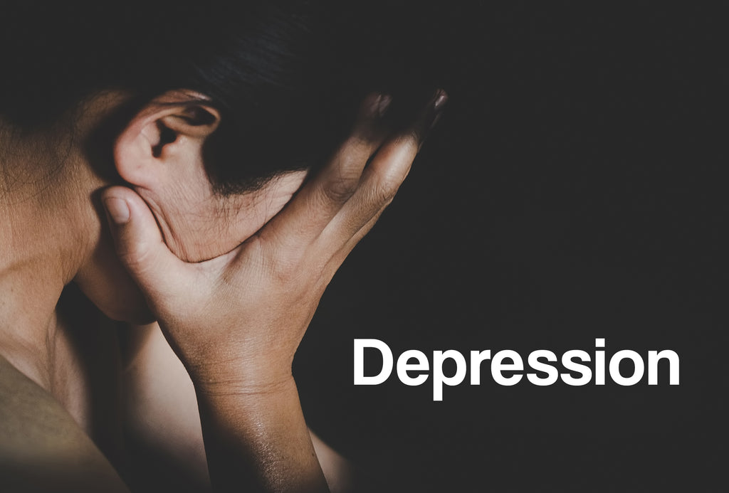 A close up of a woman resting her head in her raised right hand. The background is black. The word – Depression – can be seen