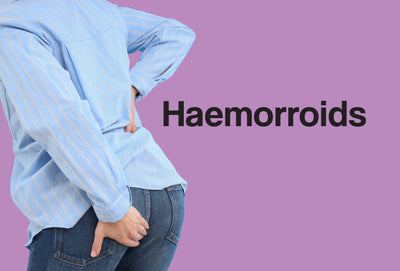 The clothed torso and bottom of a woman are visible - her body is slightly leaning forward. One hand is clasped around her bottom, although the woman is trying to 'hold something in'. The word – Haemorrhoids – can be seen