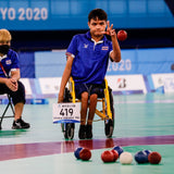 A man in a wheelchair throwing a Boccia ball at a pile of other Boccia balls