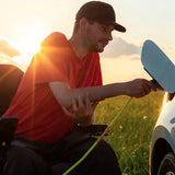 A man in a wheelchair plugging an electric charging cable into an electric car