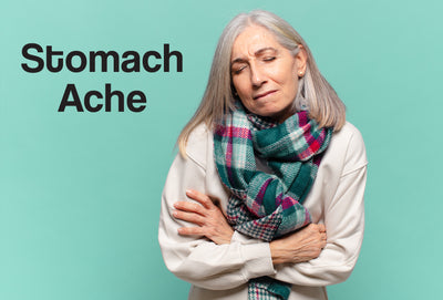 A middle age woman wearing a white top and a scarf, has both of arms and hands over her stomach – she looks like she is in a small amount of pain. The words – Stomach Ache – can be seen