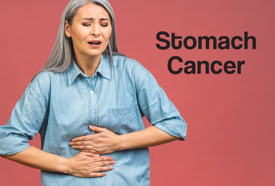 A middle age woman wearing a denim shirt has both of her hands over her stomach – she looks in pain. The words – Stomach Cancer – can be seen