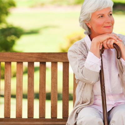 Woman sat on bench with with walking stick