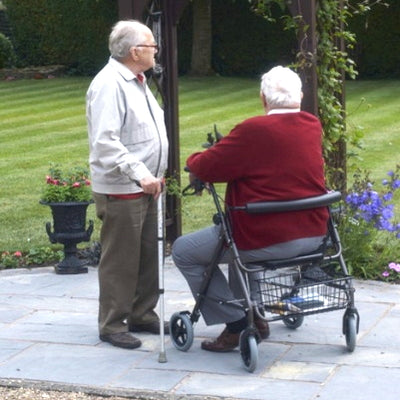 Two gentlemen, one with walking stick and one with bariatric rollator chat in a garden