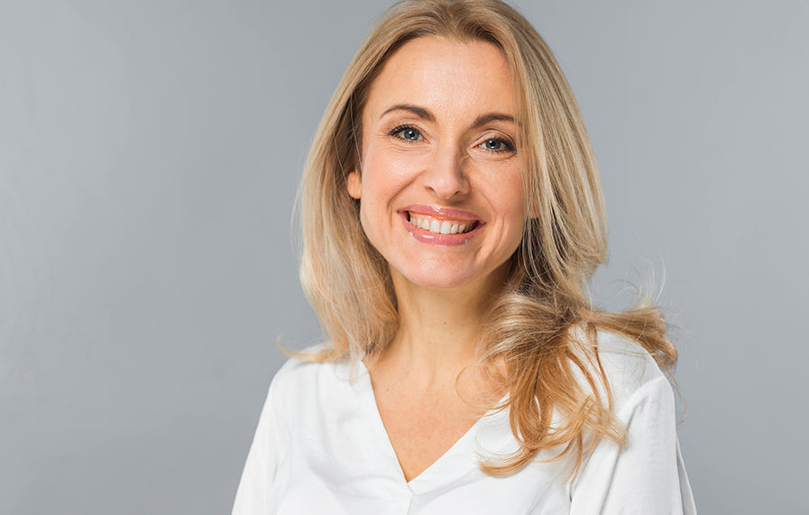 A woman with blonde hair and wearing a white top, is smiling happily out at the reader – very approachable and confident. The background is just a grey colour