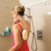 a woman standing in a shower cubicle wearing a red swimming costume, using the Homecraft Long Handled Bendable Sponge to wash her back.