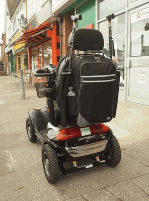 shows the Flexi Mobility Bag Large attached to the back of a mobility scooter with a walking stick/cane in either of the crutch/stick holders