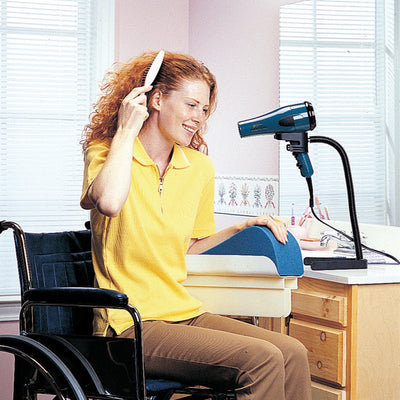 shows a young woman in a wheelchair, using the Hands Free Hair Dryer Stand to style her hair with one hand