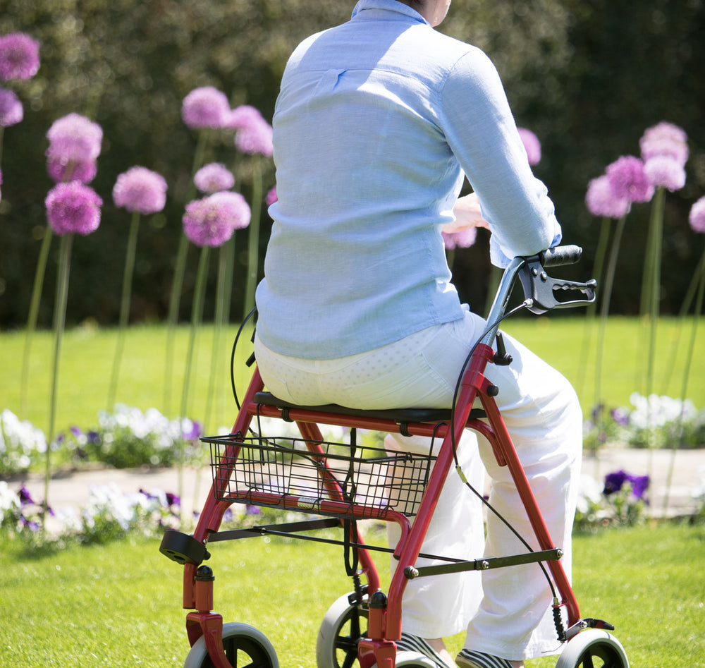 shows a woman sitting on the seat of the SR8 Steel Rollator in a garden