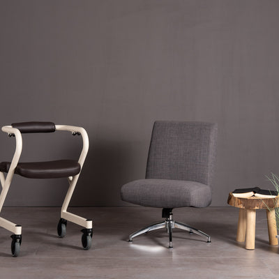 The image shows the Page Indoor Rollator with dark brown leatherette seat, alongside a chair and small coffee table