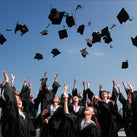 A collection of students, all dressed in gowns, throwing their graduation hats into the air