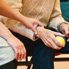 A close up of people sitting down. A hand gently rests on another person's arm in a caring position