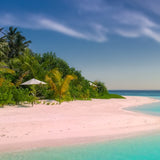 A sandy beach beside a beautiful blue sea. There are palm trees in the distance all beneath a slightly cloudy sky 