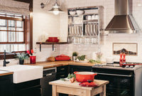 A picture of a kitchen. There's a double oven, butler sink, extractor hood, window, a plate rack and a small wooden trolley that has a crock pot on it, alongside some carrots