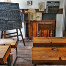 An old fashioned school room with some wooden desks and a blackboard that has some scribbles all over it