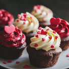 Six chocolate cupcakes on a plate. Three are topped with red icing and three are topped with white icing