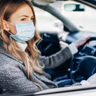 Woman, wearing a facemask, sitting in the driver's side of a car