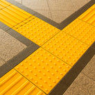Close up of bright yellow Tenji Block surrounded by pavement