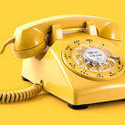An old-fashioned dialling telephone in bright yellow. The background is also bright yellow