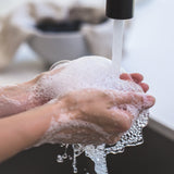 Hands covered in soap being washed under a tap with running water