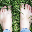 Two human feet standing on some long, green grass
