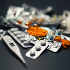 A picture of a collection of lots of different pills, along with a thermometer, all on a black background