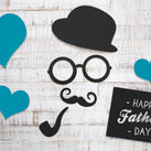 Some wooden planks painted white with 3 blue, paper hearts on top with a cut out bowler hat, glasses, moustache and a pipe. A sign says 'Happy Father's Day'