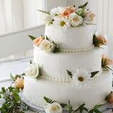 A close-up of a three tiered wedding cake with flowers on each level