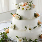 A close-up of a three tiered wedding cake with flowers on each level