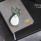 One of the PPP TAKING CARE alarms can be seen on top of a grey book that is on a black table top, The TAKING CARE logo can also be seen 
