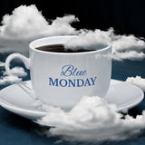 A cup and saucer. The cup is filled with black coffee. The background is dark with white clouds. The words – Blue Monday – can be seen