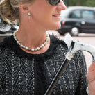 A lady wearing a smart, black top. We can see part of her face. She is holding one of the Classic Canes. In the background is a London Black Cab