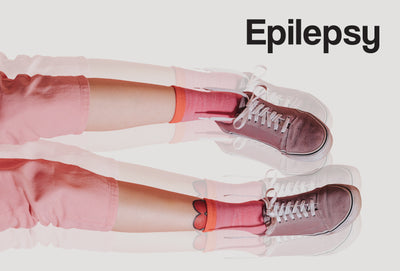 The lower half of a person. The person is wearing pink shorts, pink socks and pink trainers. The image is repeated twice, but ghosted, giving the appearance of the legs shaking. The word – Epilepsy – can be seen