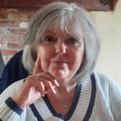 A close-up of Lesley. She sits in front of a brick fireplace and is resting her head on her hands