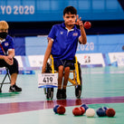  A man in a wheelchair throwing a Boccia ball at a pile of other Boccia balls