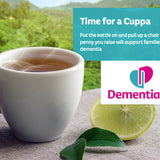 A steaming cup of tea on a wooden table; in the background is a tea plantation. The Dementia UK logo can be seen, as well as a small amount of text about – Time For A Cuppa
