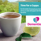 A steaming cup of tea on a wooden table; in the background is a tea plantation. The Dementia UK logo can be seen, as well as a small amount of text about – Time For A Cuppa