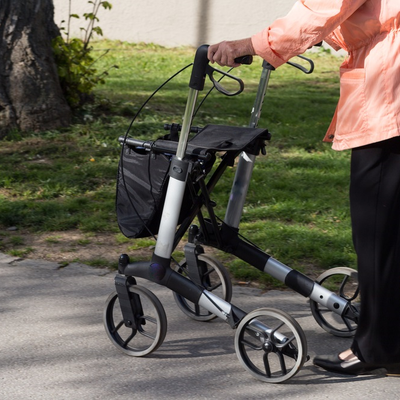 Lady strolls through the park with a four wheel rollator