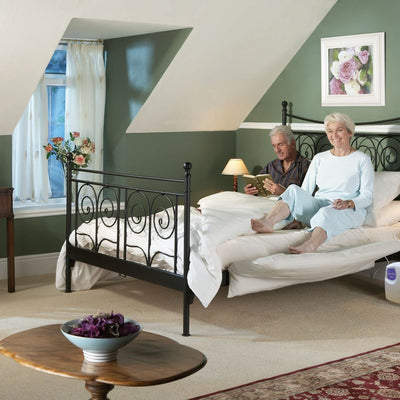 Older couple sat in bed while woman uses electronic leg lifter