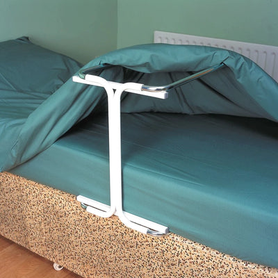 A blanket cradle in use in a single bed. A green quilt is lying on top of it