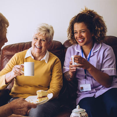 Female carer and two senior ladies laugh while having tea and cake