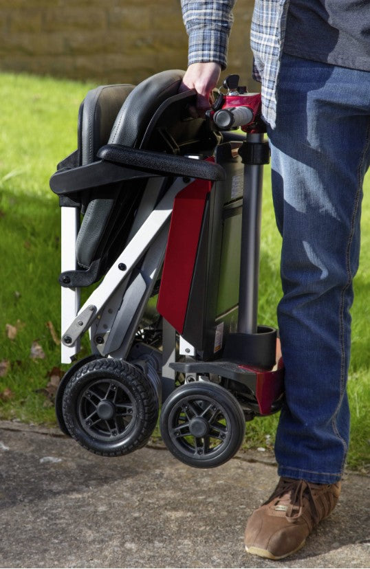 A man holding a folded up red Manual Fold+ Scooter outside
