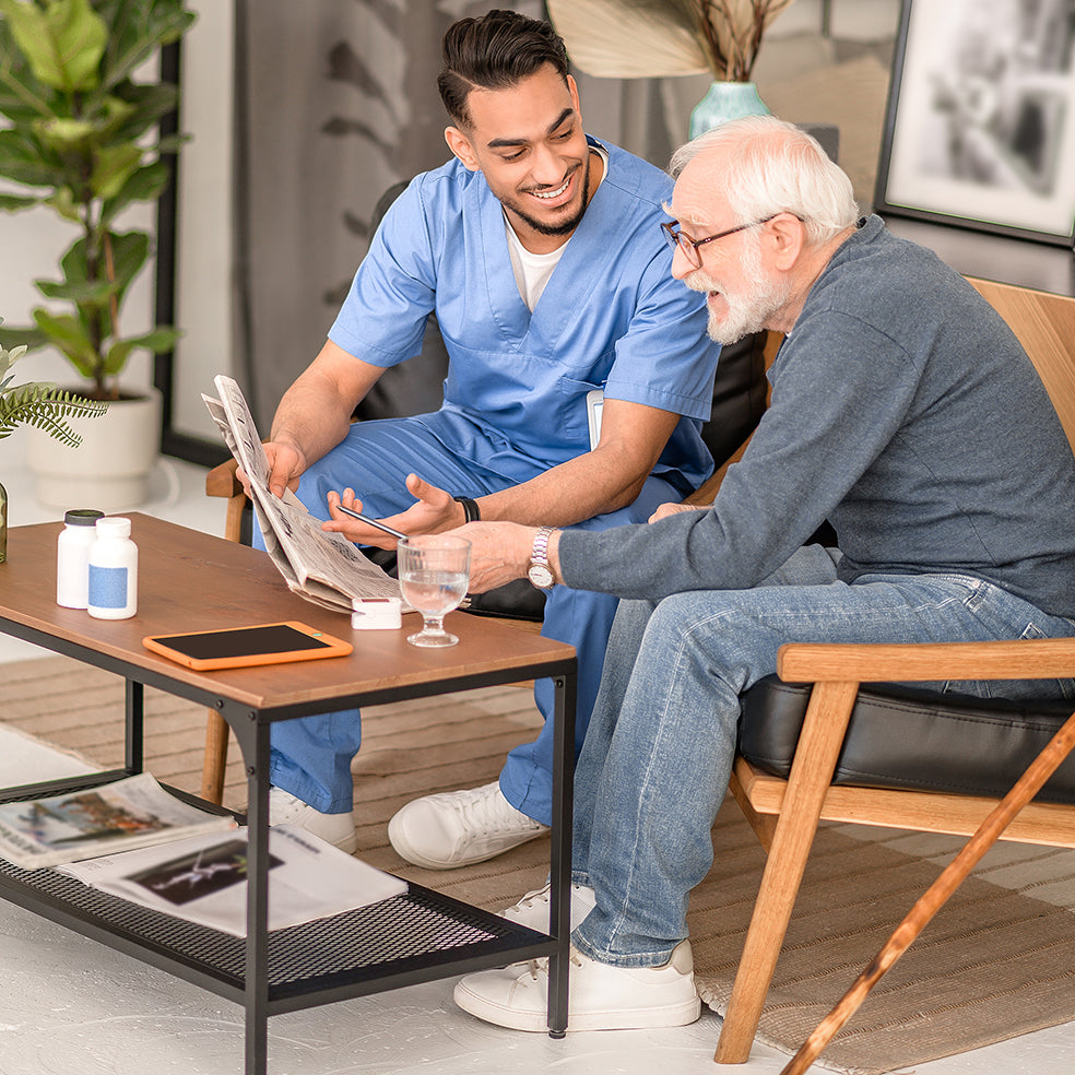 An elderly man is sitting in a chair. Anther man (wearing 