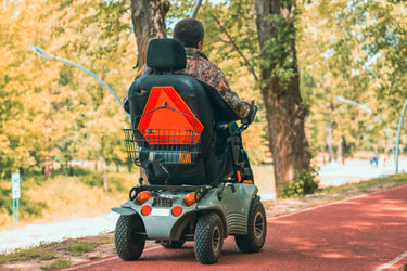 The back view of a man driving a mobility scooter through a park