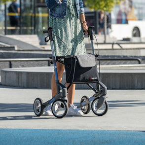 A woman with a rollator standing in a public place outdoors.